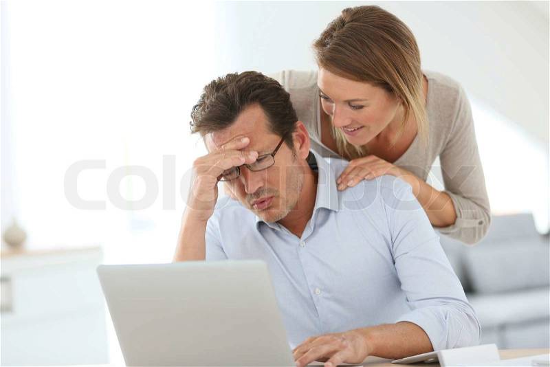 Woman trying to relax worried husband in front of laptop, stock photo