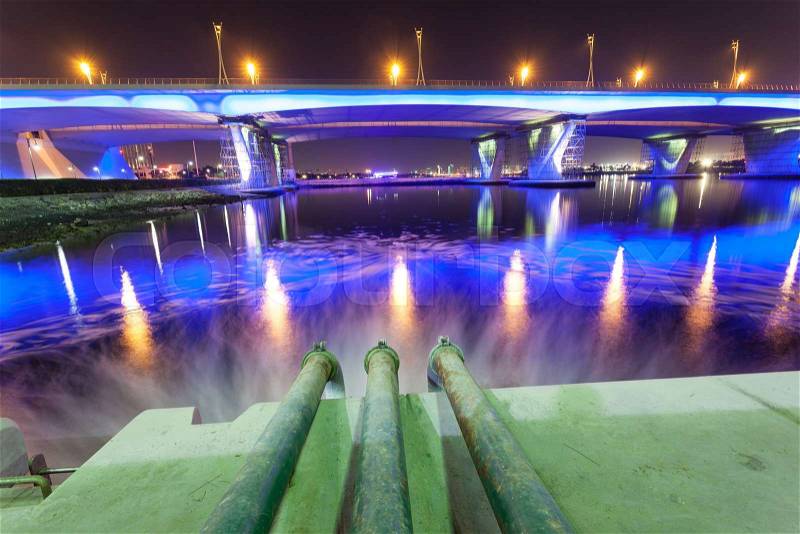 Sewage pipes discharging water into the Dubai Creek at night. Dubai, United Arab Emirates, stock photo