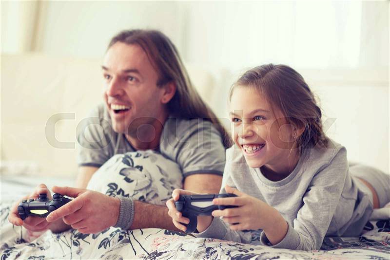 Child playing video game on tv with father in morning at bed at home, stock photo