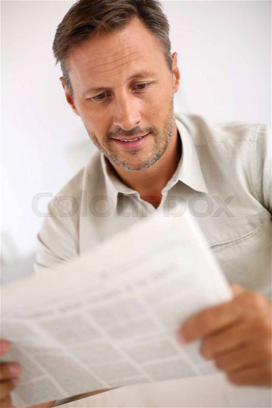 Relaxed handsome man at home reading newspaper, stock photo