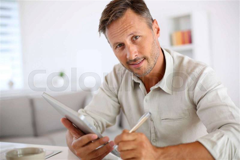 Man reading news on both paper and digital tablet, stock photo