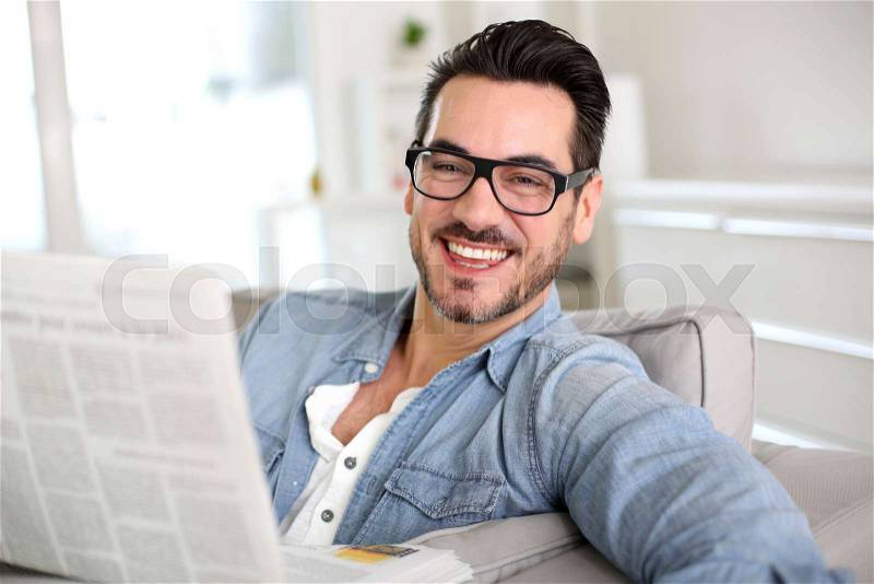 Cheerful guy reading newspaper in sofa, stock photo