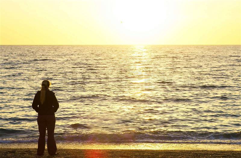 Female silhouette on seacoast against the sunset sky, stock photo