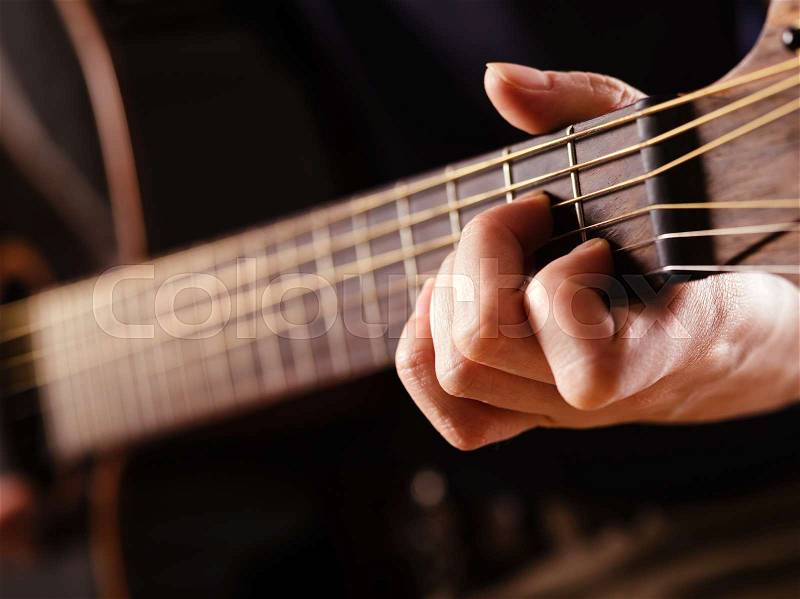 Photo of a woman playing an acoustic guitar with extreme shallow depth of field with focus on hand and headstock, stock photo