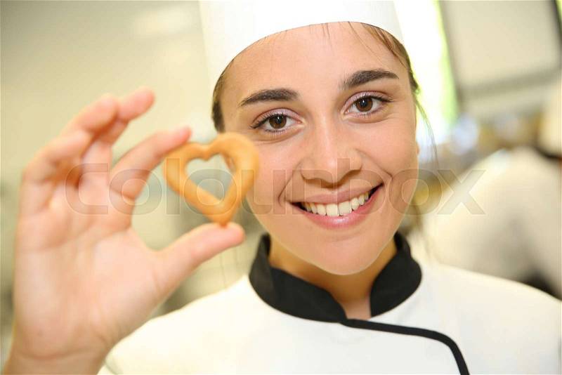 Portrait of young pastry cook holding cookie, stock photo