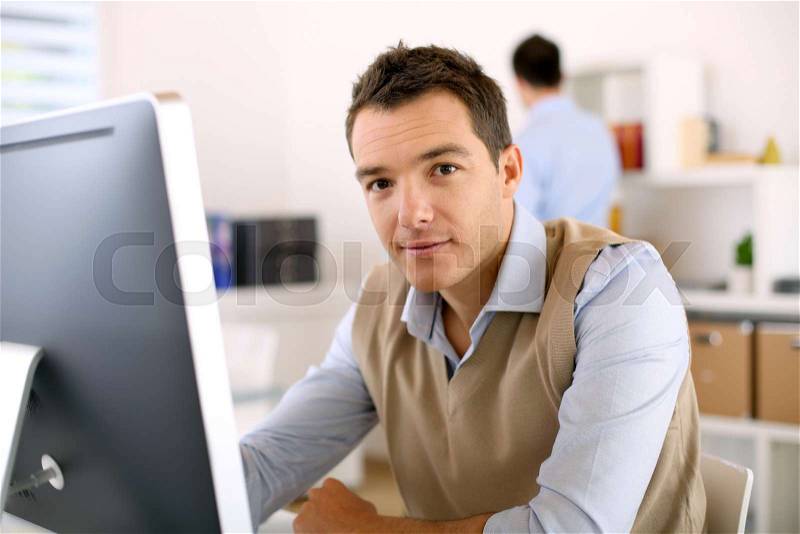 Man working in office in front of desktop computer, stock photo