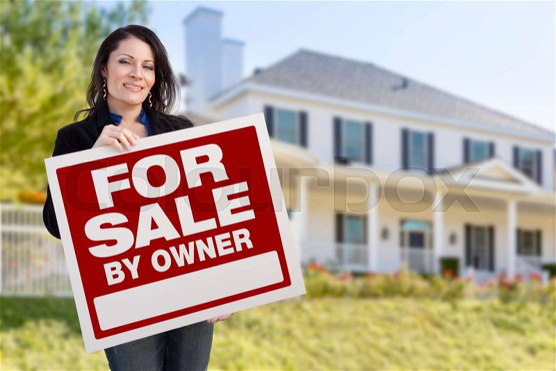 Smiling Hispanic Female Holding For Sale By Owner Sign In Front of Beautiful House, stock photo