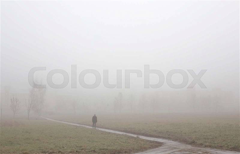 Foggy cold weather, lonely man walking along the road, stock photo