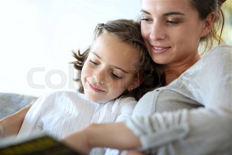 Mom with little girl reading book in sofa, stock photo