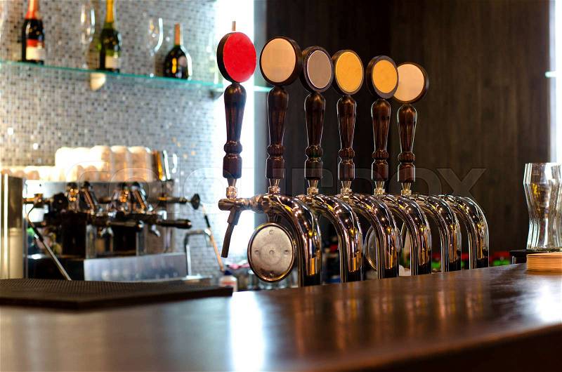 Beer taps behind a deserted bar counter for dispensing draft beer from a large storage keg below the wooden counter, stock photo