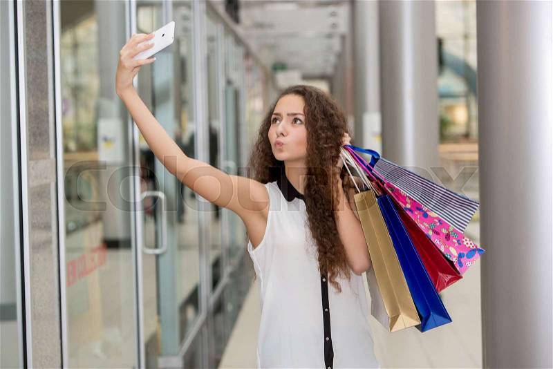 Beautiful young woman goes shopping using a smartphone with a shopping bags in the mall, stock photo