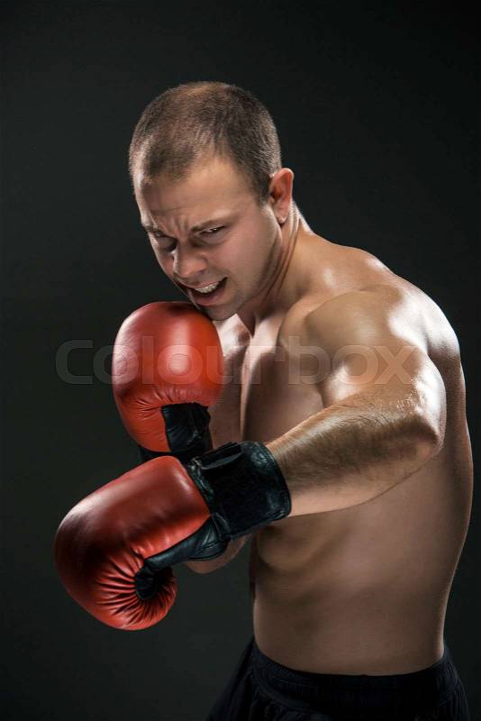 Young boxer in red gloves boxing over black background, stock photo