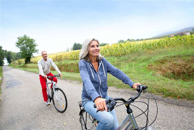 Senior couple riding bicycle in countryside, stock photo