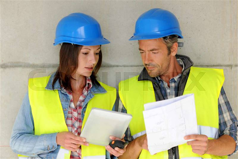 Construction team standing against building wall with blueprint, stock photo