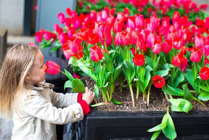 Little adorable girl near red flowers in New York streets, stock photo