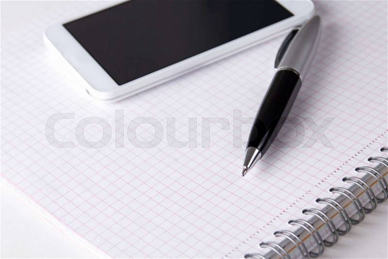 Close up of note book with checked pages, pen and smart phone, stock photo