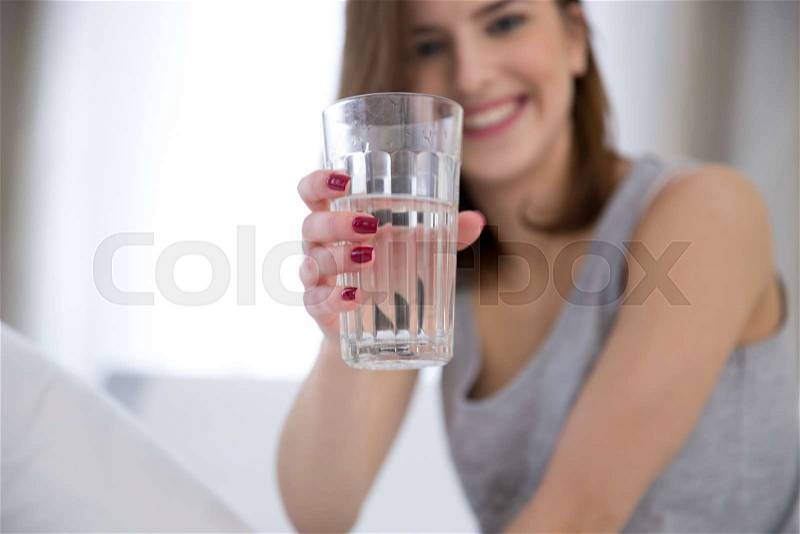 Portrait of a happy woman holding glass of water. Focus on glass, stock photo