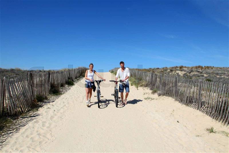 Couple walking on a sandy path with bicycles, stock photo