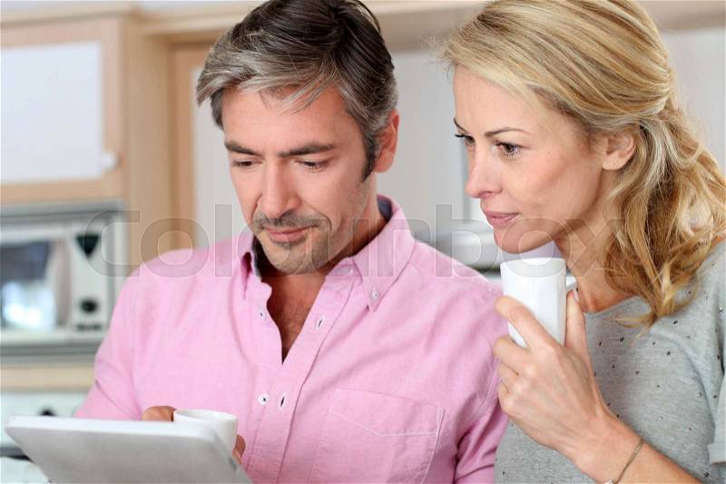 Middle aged couple using tablet in kitchen, stock photo