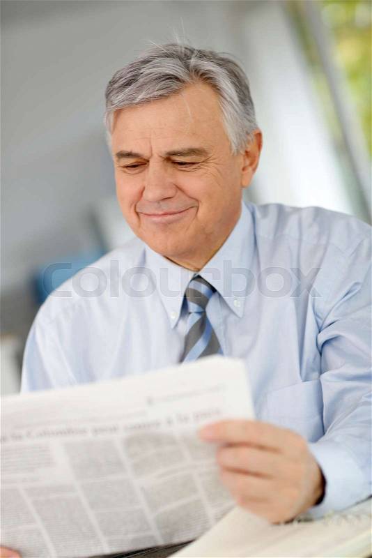 Portrait of senior businessman reading newspaper, stock photo