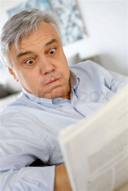 Senior man reading newspaper with puzzled look, stock photo