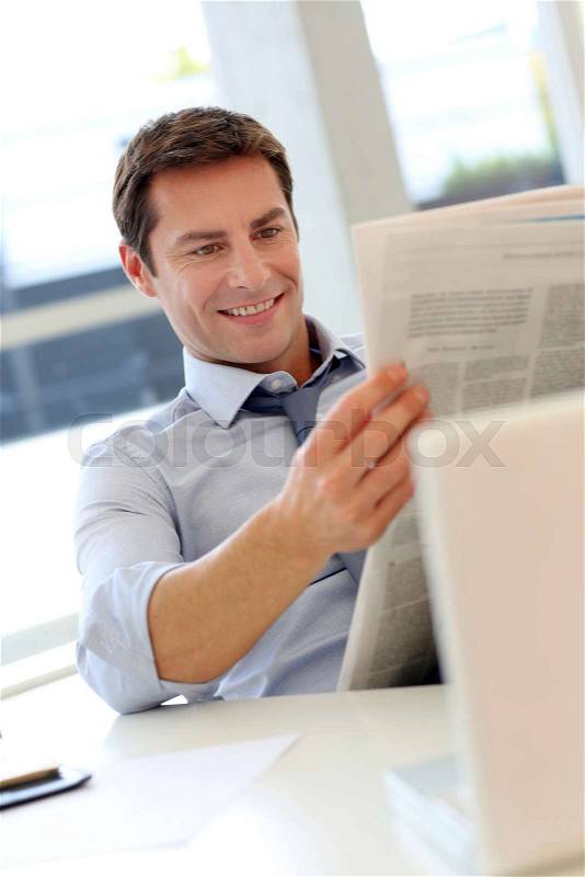 Businessman reading newspaper in office, stock photo