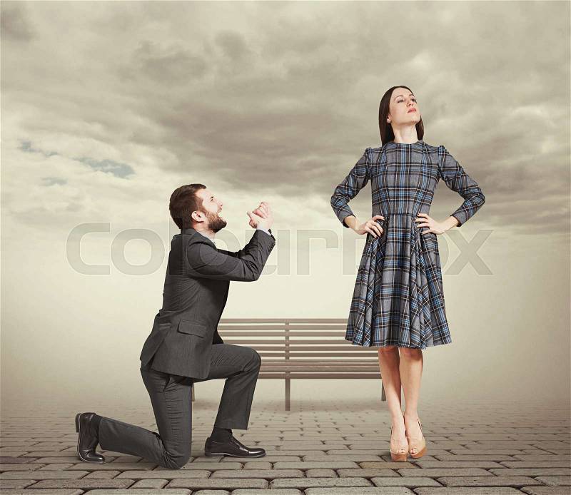 Sad man kneeling on one knee, looking at young attractive woman and asking for forgiveness. photo at outdoor, stock photo