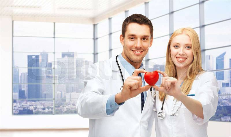 Medicine, cardiology, healthcare and people concept - happy young doctors cardiologists with red heart over clinic background, stock photo
