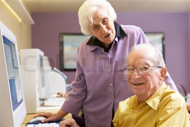 Senior woman helping senior man use computer, stock photo