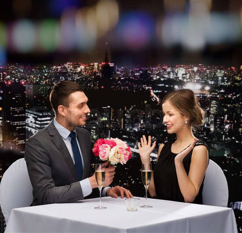 Restaurant, couple and holiday concept - smiling man giving flower bouquet to woman at restaurant, stock photo