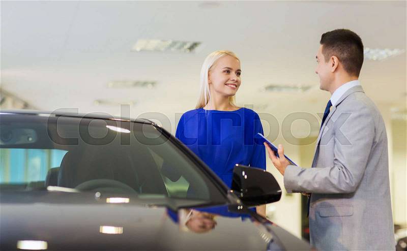 Auto business, car sale, consumerism and people concept - happy woman with dealer talking in auto show or salon, stock photo