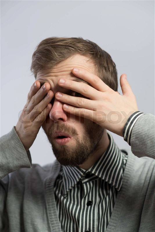 Young man closes his eyes with his hands, stock photo