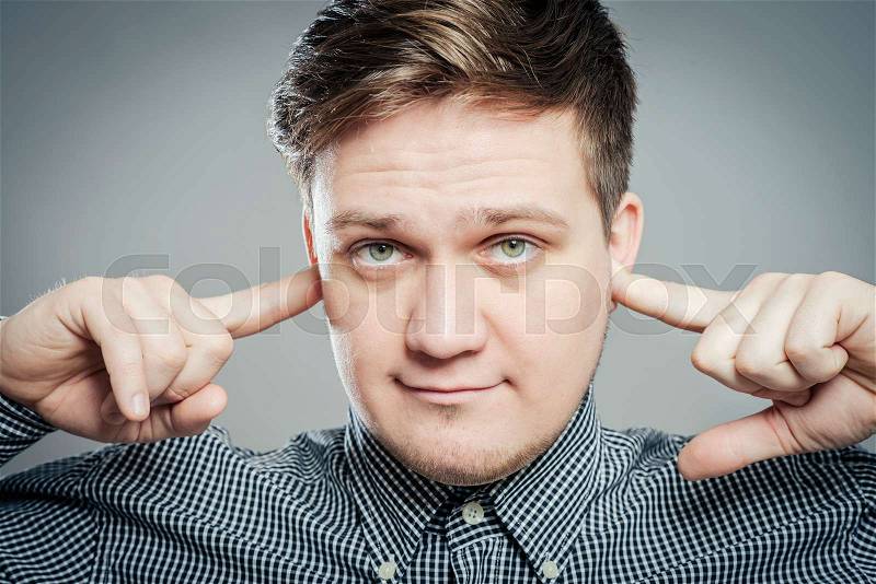 Young man shows he does not want to hear . Fingers in his ears, stock photo