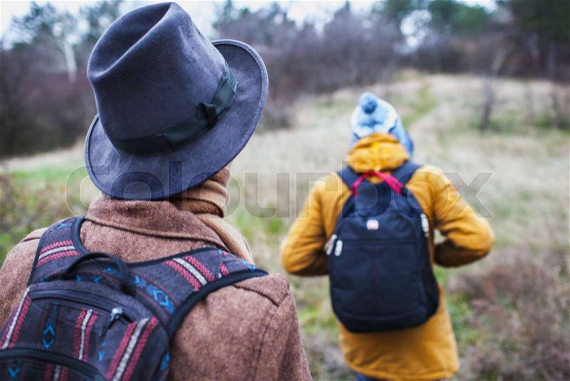 Hiker wearing hiking backpack and jacket on hike in forest. Man wearing hat gloves using poles outdoors in woods. Male hiker standing looking away, stock photo