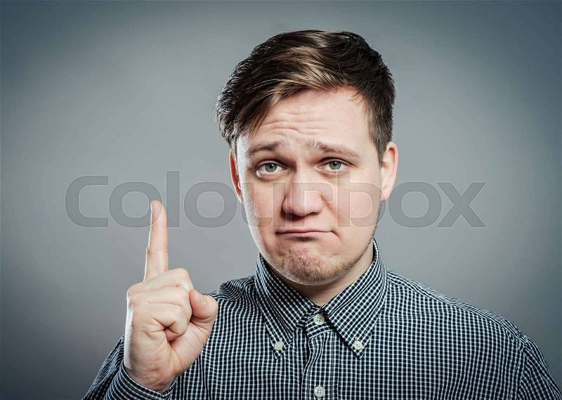 Portrait of disappointed young man pointing upwards while standing against gray background. Vertical shot, stock photo