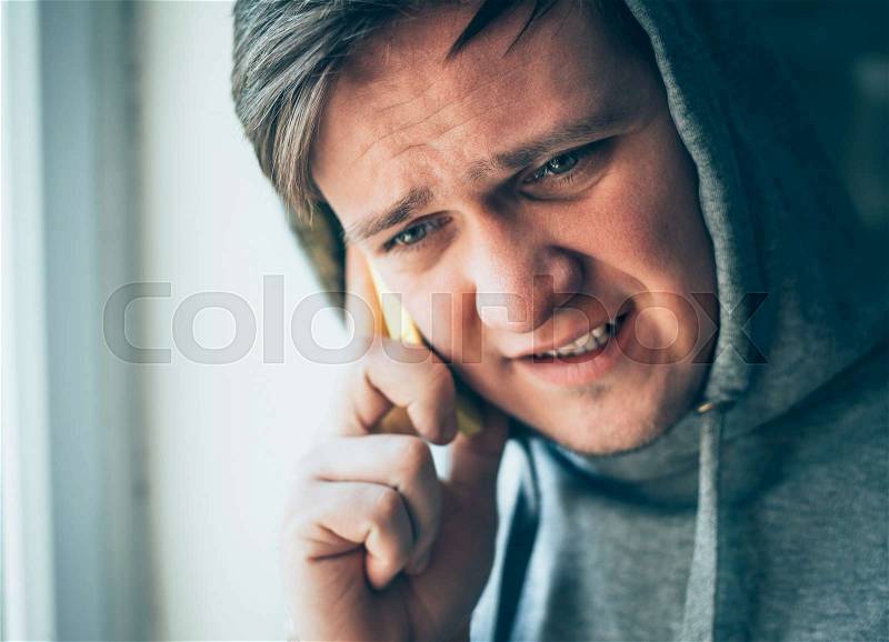 The hooded man talking on the phone at the window, stock photo