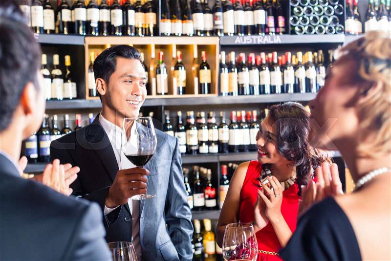 Asian friends toasting with red wine in bar, stock photo