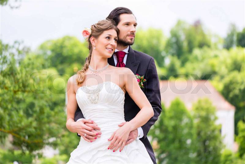 Wedding bride and groom outside in the garden, groom embracing bride, stock photo
