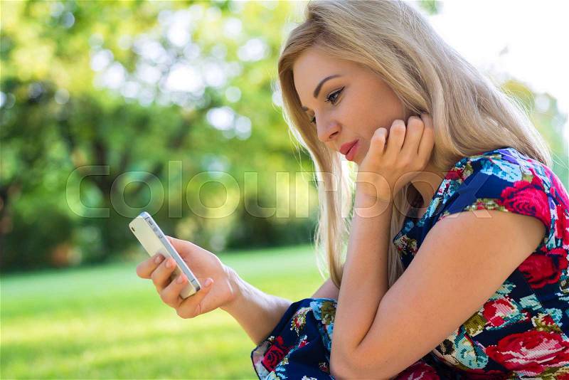 Woman in park online dating with smart phone, stock photo