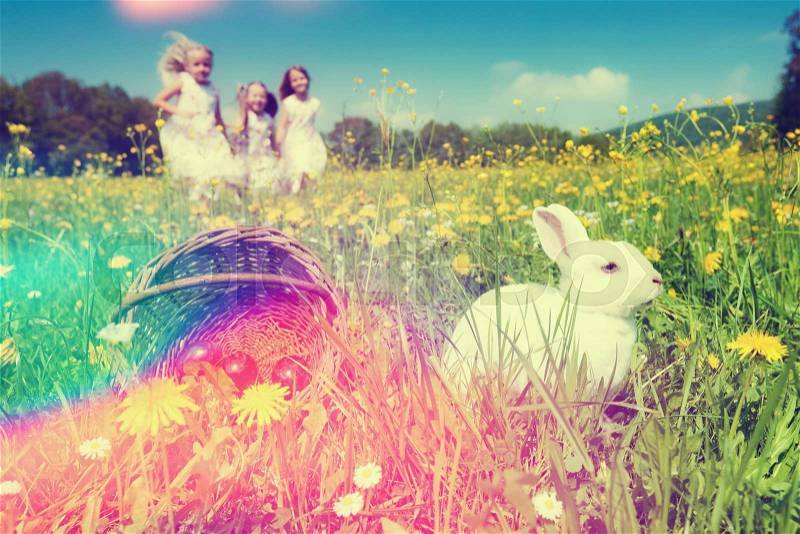 Children on an Easter Egg hunt on a meadow in spring, in the foreground the Easter bunny is waiting, stock photo