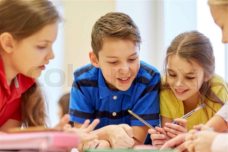 Education, elementary school, learning and people concept - group of school kids with pens and papers writing in classroom, stock photo