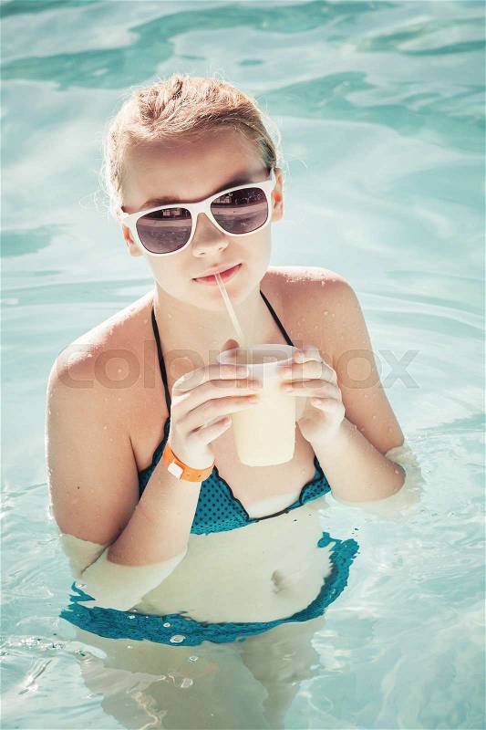 Little blond girl drinks cocktail in swimming pool, vintage toned photo filter effect, stock photo