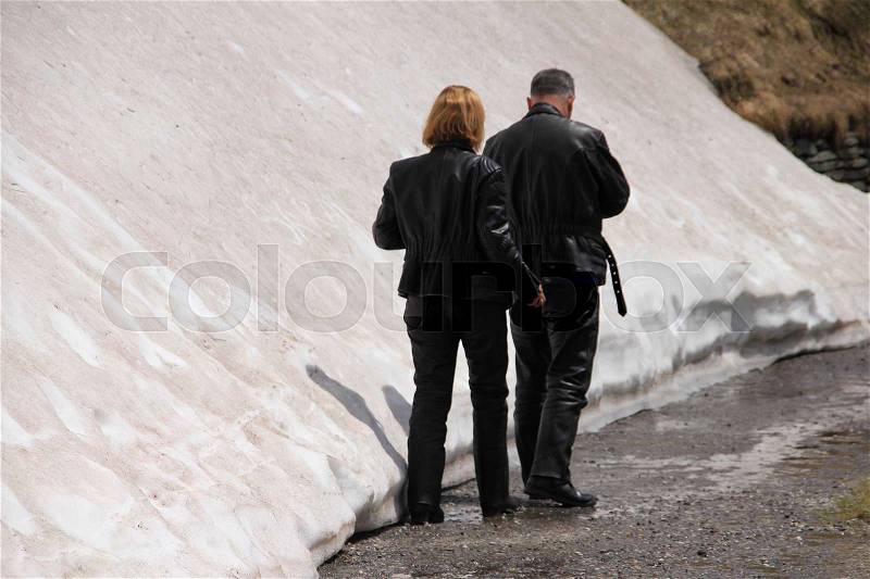 Couple, man and wife, in leather motorcycle suit walks in the snow at the top of the Grossglockner in the summer in Austria, stock photo