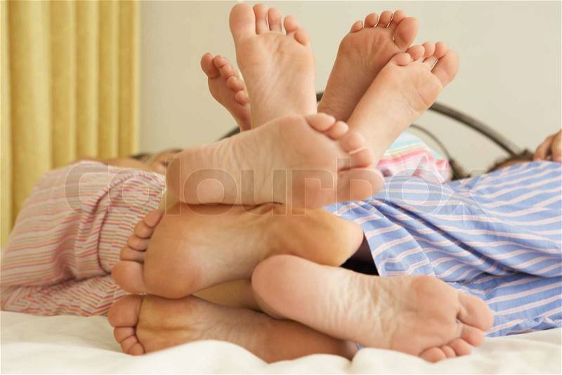 Close Up Of Family's Feet Relaxing On Bed At Home, stock photo