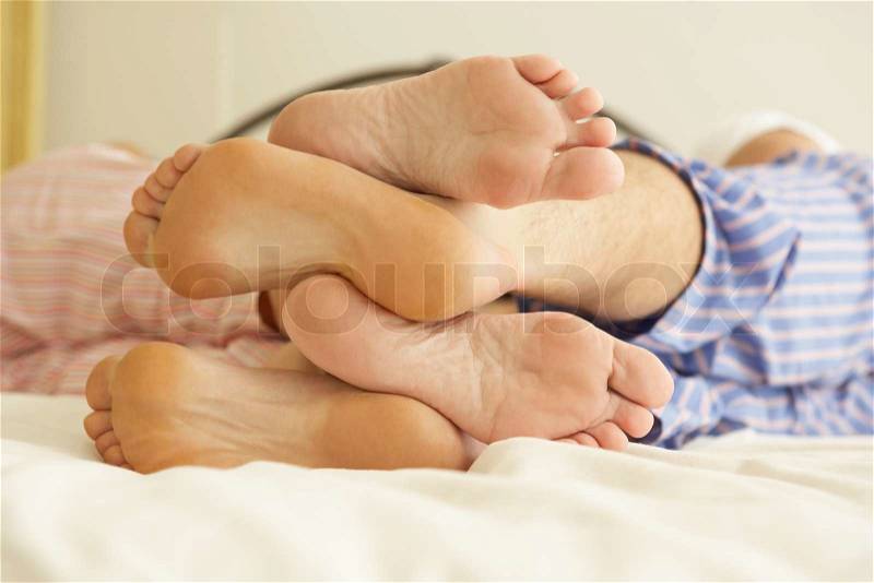 Close Up Of Couple\'s Feet Relaxing On Bed At Home, stock photo