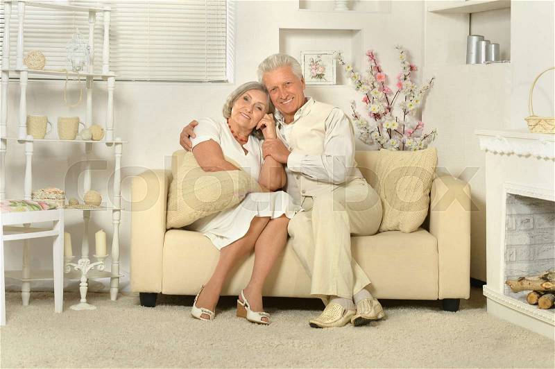 Two elderly people sitting at home on couch, stock photo