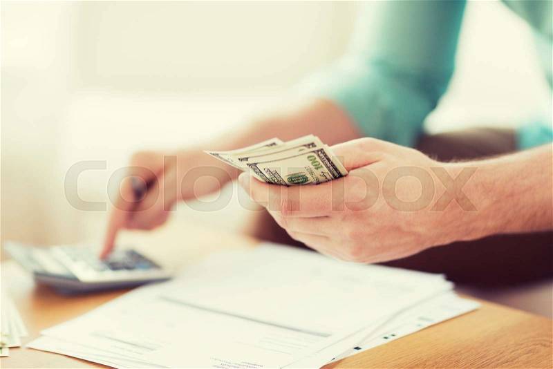 Savings, finances, economy and home concept - close up of man with calculator counting money and making notes at home, stock photo