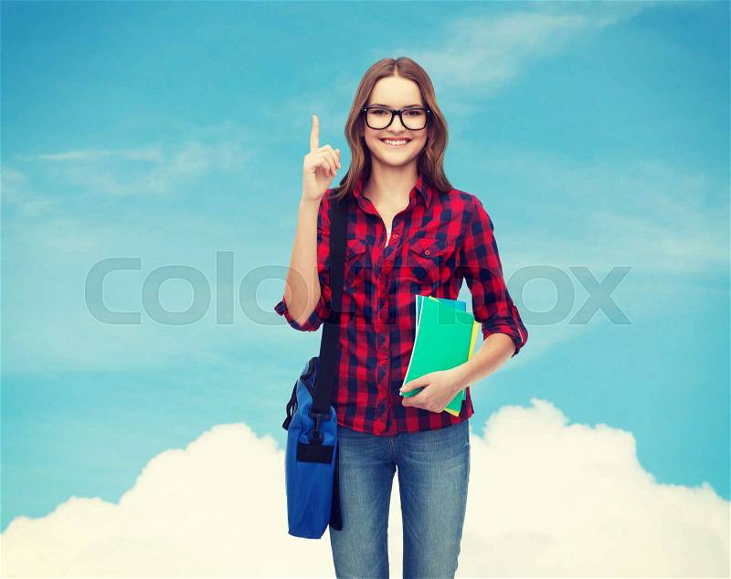 Education and people concept - smiling female student in eyeglasses with bag and notebooks showing finger up over blue sky background, stock photo