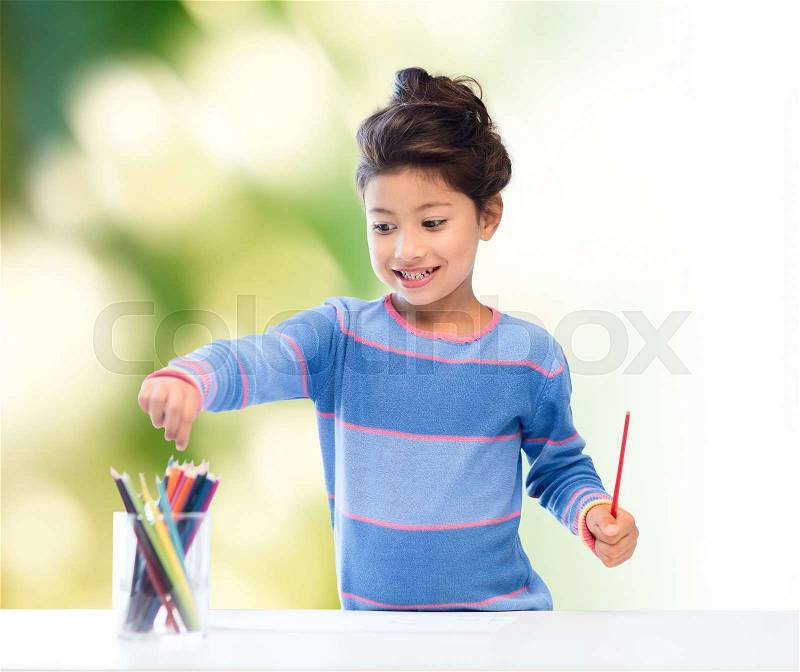 Children, creativity and happy people concept - happy little girl drawing with coloring pencils over green background, stock photo