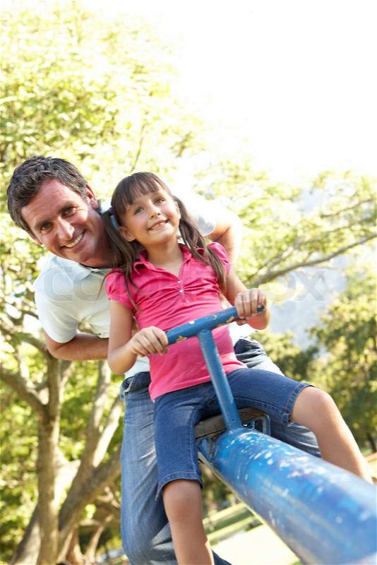 Father And Daughter Riding On See Saw In Playground, stock photo
